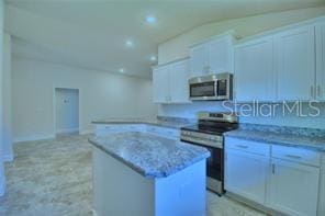 kitchen with white cabinets, stainless steel appliances, a center island, and light stone countertops