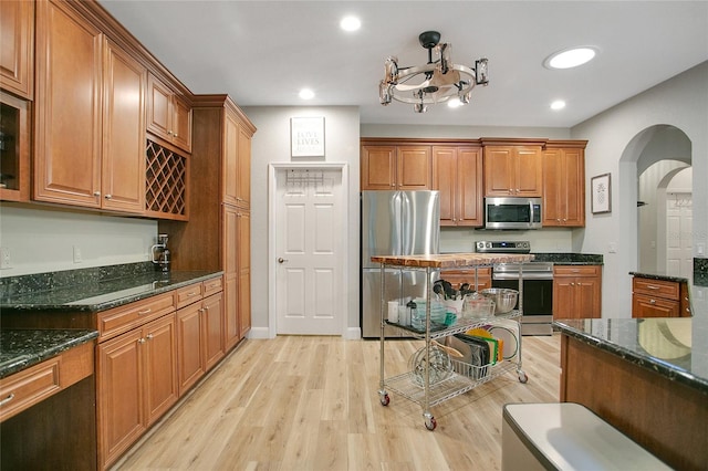 kitchen with stainless steel appliances, dark stone counters, and light wood-type flooring