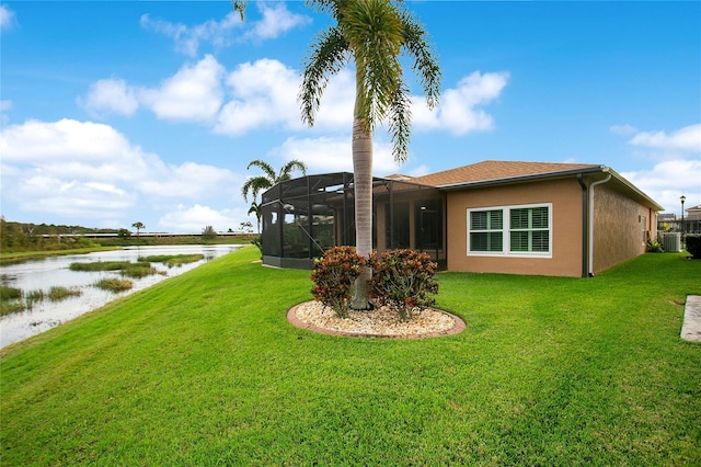 back of property with a water view, central air condition unit, glass enclosure, and a lawn