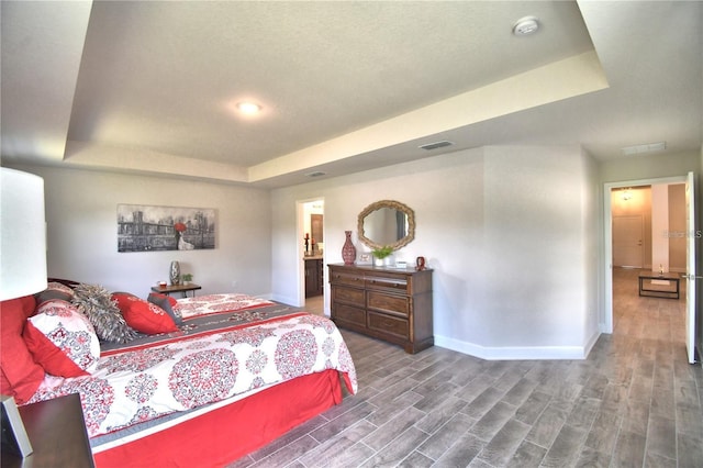 bedroom featuring ensuite bathroom, a tray ceiling, and hardwood / wood-style flooring