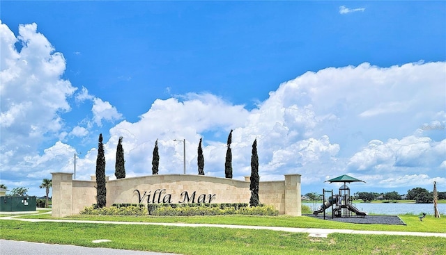 community / neighborhood sign featuring a water view and a lawn