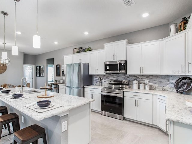 kitchen featuring white cabinets, pendant lighting, appliances with stainless steel finishes, and a kitchen island with sink