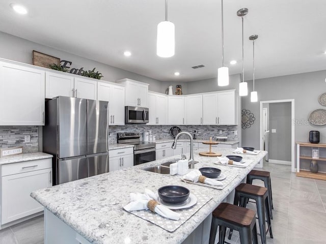 kitchen with stainless steel appliances, pendant lighting, a kitchen island with sink, and decorative backsplash