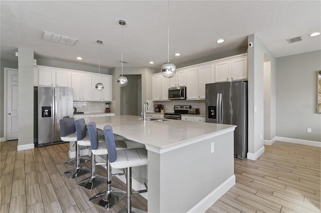 kitchen featuring stainless steel appliances, white cabinetry, a center island with sink, and pendant lighting