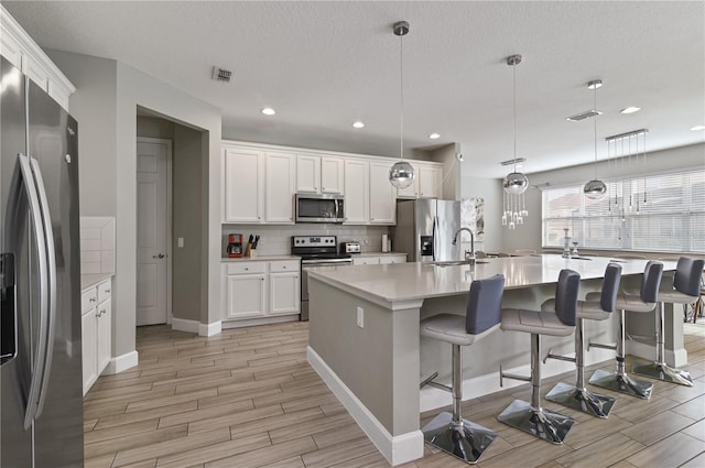 kitchen featuring hanging light fixtures, a center island with sink, white cabinetry, and appliances with stainless steel finishes