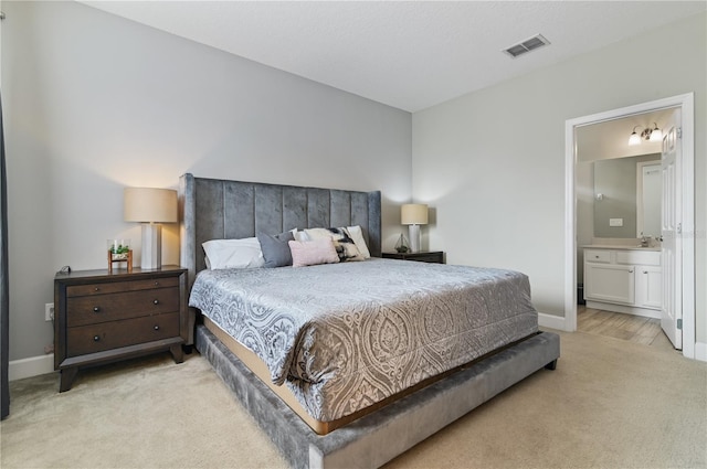 bedroom with ensuite bathroom, light colored carpet, and sink