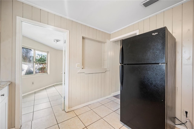 kitchen with wooden walls, black refrigerator, and light tile patterned floors