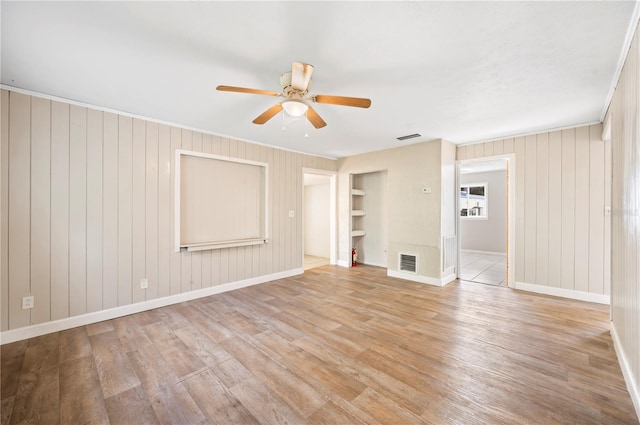 interior space with built in shelves, light wood-type flooring, ceiling fan, and wood walls