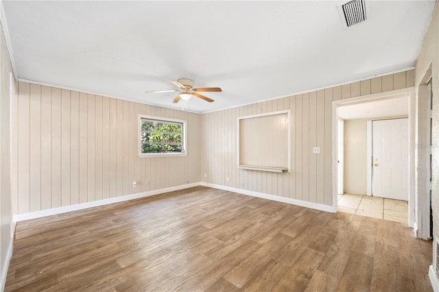 spare room featuring hardwood / wood-style floors, ornamental molding, ceiling fan, and wooden walls