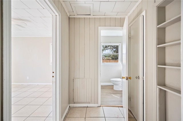 hallway featuring ornamental molding, built in shelves, wood walls, and light tile patterned flooring