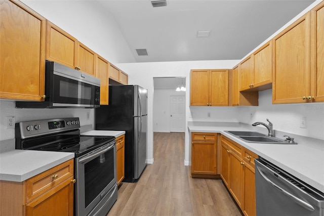 kitchen with appliances with stainless steel finishes, sink, vaulted ceiling, and light hardwood / wood-style flooring