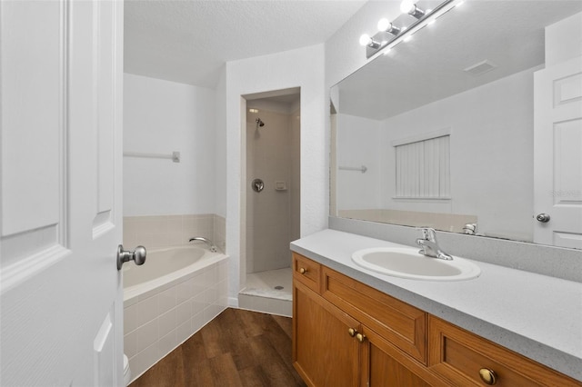 bathroom featuring wood-type flooring, vanity, shower with separate bathtub, and a textured ceiling