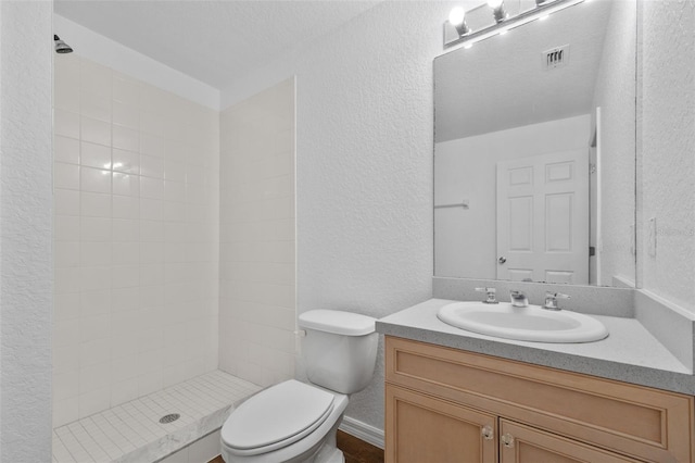 bathroom featuring vanity, toilet, a textured ceiling, and tiled shower