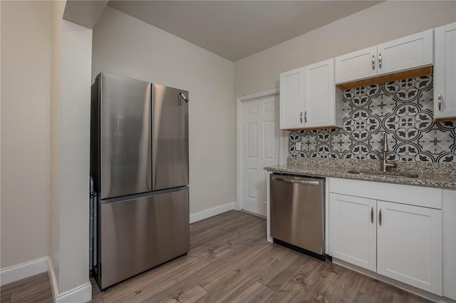 kitchen featuring stainless steel appliances, light wood-type flooring, white cabinets, light stone counters, and sink