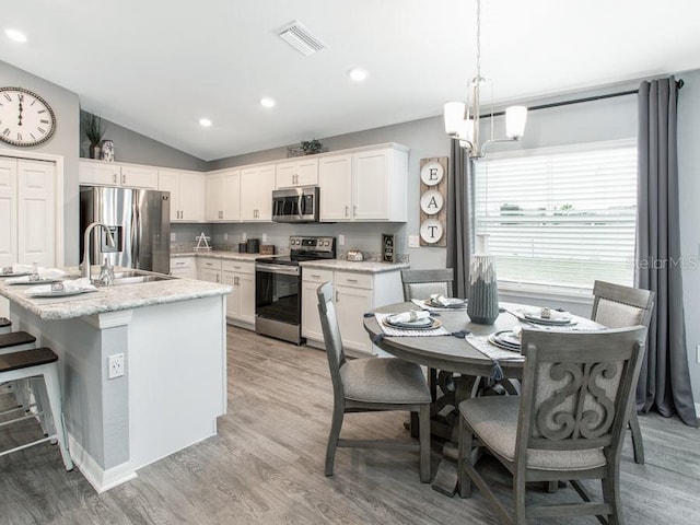 kitchen with stainless steel appliances, white cabinetry, an island with sink, and vaulted ceiling