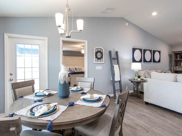 dining area featuring light wood-type flooring, ceiling fan with notable chandelier, and vaulted ceiling