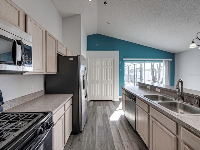 kitchen with light brown cabinetry, stainless steel appliances, lofted ceiling, and sink