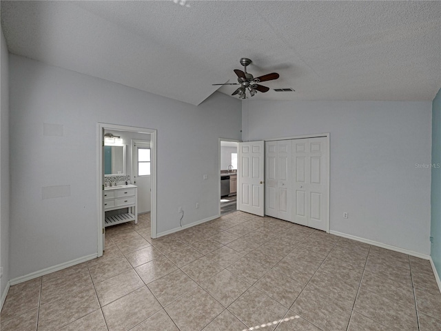 unfurnished bedroom featuring ensuite bathroom, vaulted ceiling, ceiling fan, light tile patterned floors, and a closet