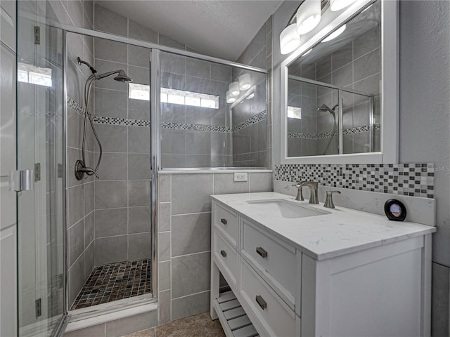 bathroom featuring vanity, vaulted ceiling, a textured ceiling, walk in shower, and tile walls