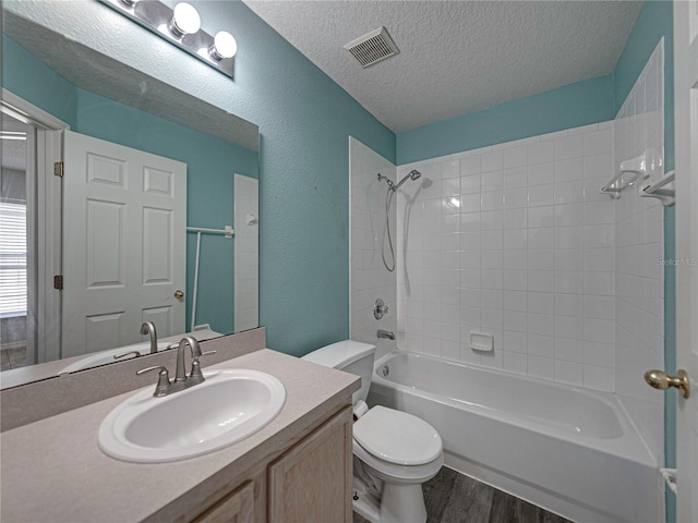 full bathroom with wood-type flooring, a textured ceiling, toilet, vanity, and tiled shower / bath