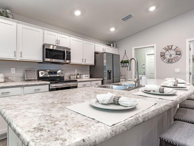 kitchen featuring stainless steel appliances, a center island with sink, sink, a kitchen bar, and white cabinets