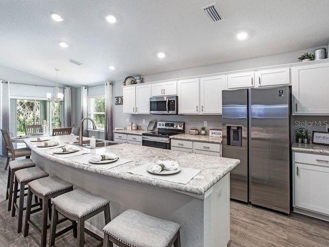 kitchen featuring vaulted ceiling, white cabinets, sink, appliances with stainless steel finishes, and decorative light fixtures