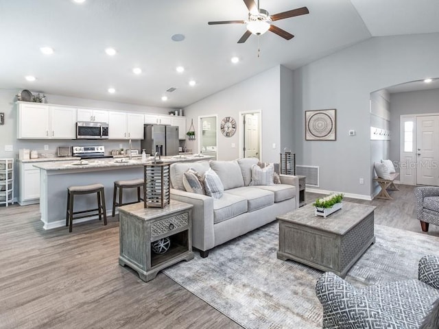 living room featuring ceiling fan, light wood-type flooring, and lofted ceiling