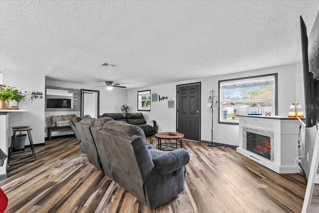 living room featuring ceiling fan, wood-type flooring, a high end fireplace, and a textured ceiling