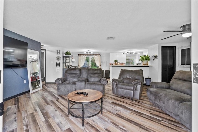 living room with a textured ceiling, ceiling fan, and wood-type flooring