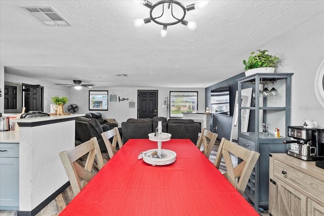 dining space with a textured ceiling, a healthy amount of sunlight, and ceiling fan with notable chandelier