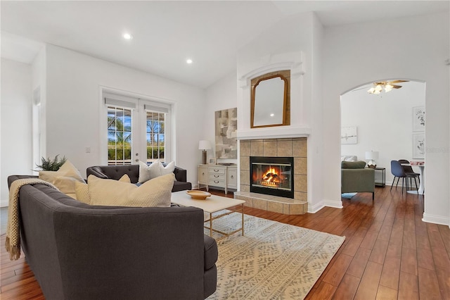 living room featuring ceiling fan, a tiled fireplace, french doors, wood-type flooring, and vaulted ceiling