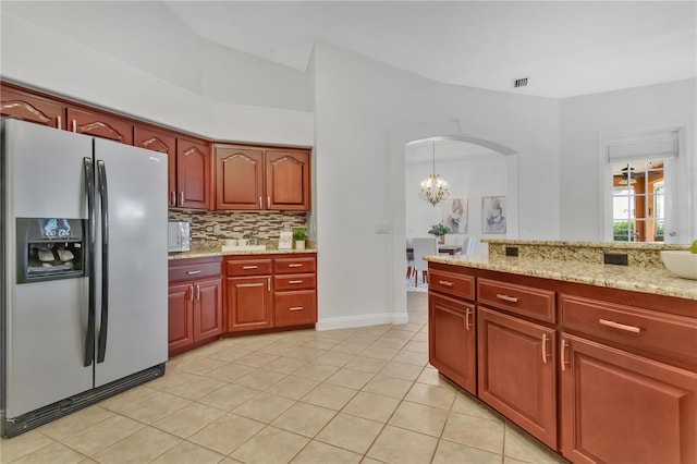 kitchen featuring decorative backsplash, light tile patterned floors, stainless steel fridge, light stone counters, and a chandelier