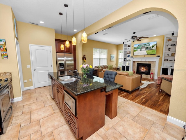 kitchen featuring a center island with sink, stainless steel appliances, pendant lighting, a tiled fireplace, and sink