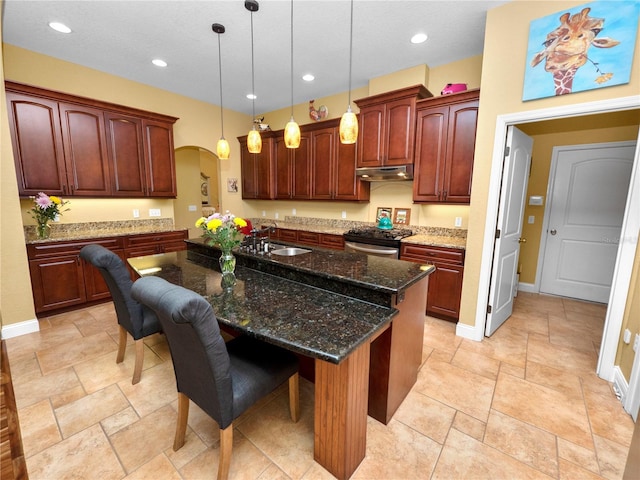 kitchen with a center island with sink, decorative light fixtures, stainless steel range, a kitchen breakfast bar, and dark stone countertops