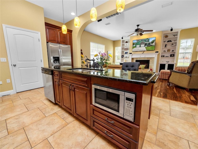 kitchen featuring sink, a tile fireplace, a kitchen island with sink, pendant lighting, and appliances with stainless steel finishes