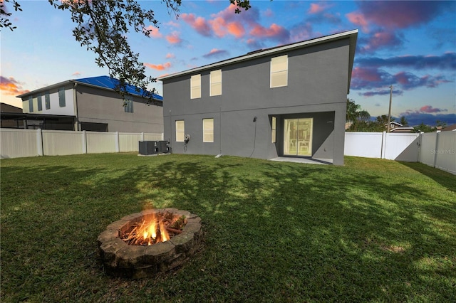 back house at dusk featuring a fire pit, a yard, and central AC