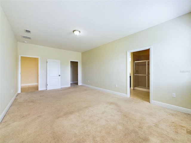 unfurnished bedroom with a walk in closet, ensuite bathroom, a closet, and light colored carpet