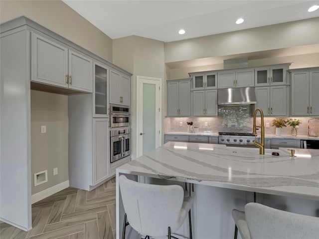 kitchen with light parquet floors, backsplash, ventilation hood, and light stone counters