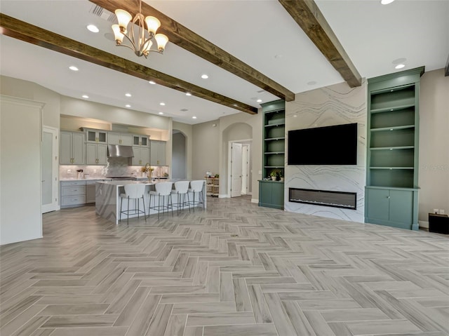 10469 Meadowrun Dr, Lithia, FL 33547 - living area with arched walkways, beamed ceiling, a chandelier, a glass covered fireplace, and built in shelves