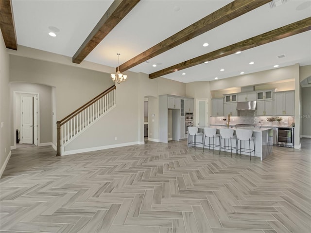 unfurnished living room with beamed ceiling, light parquet flooring, an inviting chandelier, and wine cooler