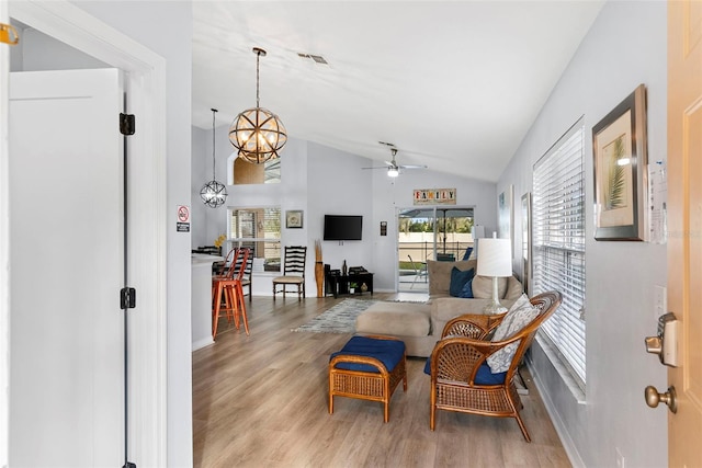 living room featuring ceiling fan with notable chandelier, vaulted ceiling, and light wood-type flooring