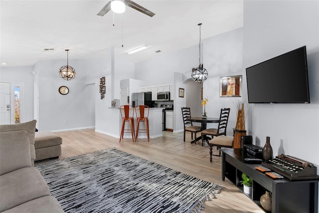 living room featuring ceiling fan with notable chandelier, light wood-type flooring, and high vaulted ceiling