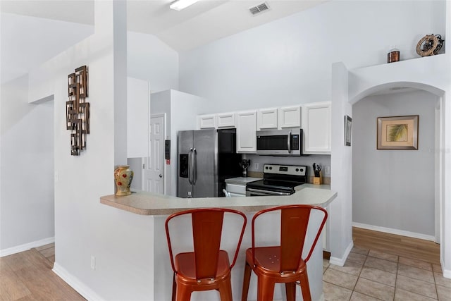 kitchen featuring kitchen peninsula, lofted ceiling, a breakfast bar, white cabinets, and appliances with stainless steel finishes