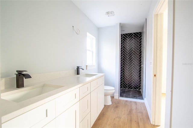 bathroom featuring a tile shower, vanity, hardwood / wood-style flooring, and toilet