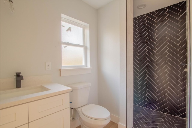 bathroom featuring a tile shower, vanity, and toilet