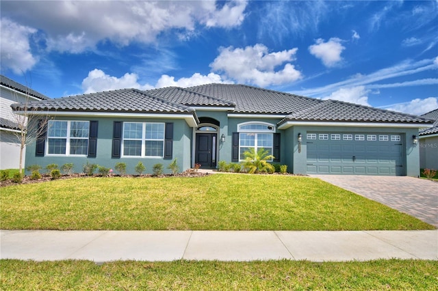 ranch-style home with decorative driveway, stucco siding, a garage, a tiled roof, and a front lawn