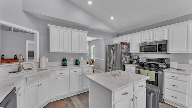 kitchen featuring appliances with stainless steel finishes, light wood-type flooring, sink, white cabinetry, and lofted ceiling