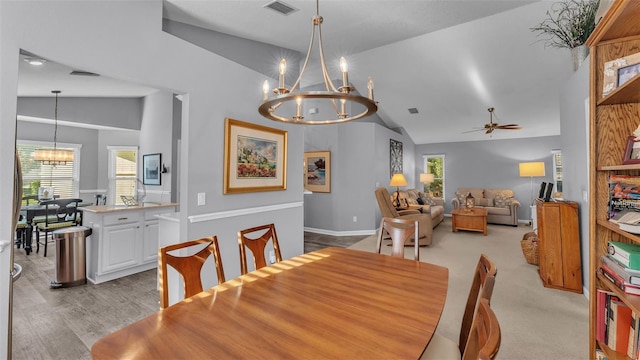 dining area featuring ceiling fan with notable chandelier, lofted ceiling, and light carpet