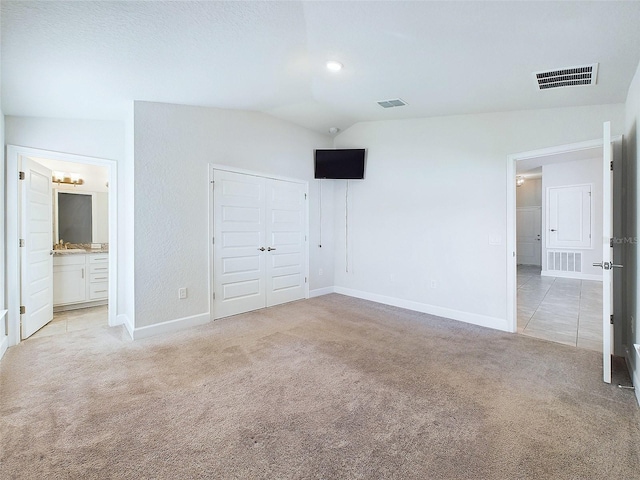 unfurnished bedroom with ensuite bathroom, vaulted ceiling, light colored carpet, and a closet