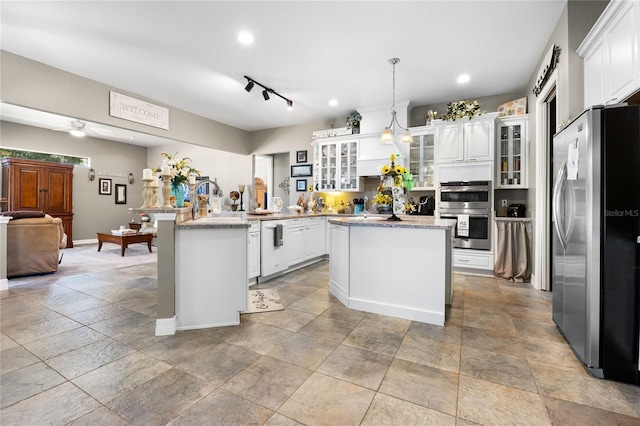 kitchen with light stone countertops, appliances with stainless steel finishes, pendant lighting, white cabinetry, and an island with sink